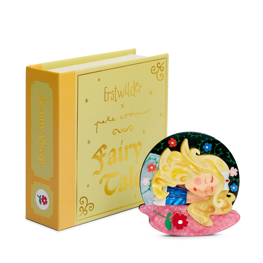 Yellow book with decorative cover and sleeping beauty brooch figurine on a white background
