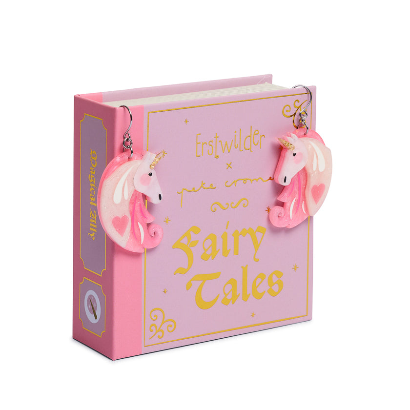 Pink book titled 'Fairy Tales' with unicorn earrings on a white background