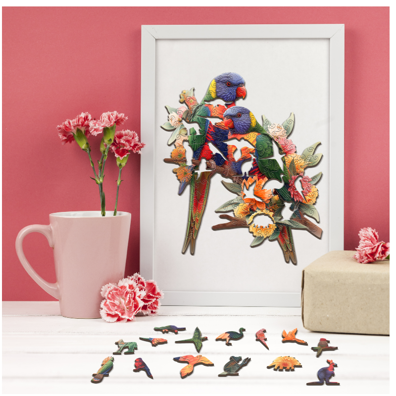 Framed artwork of colorful birds and flowers next to a pink mug with flowers and scattered bird figurines on a white surface.