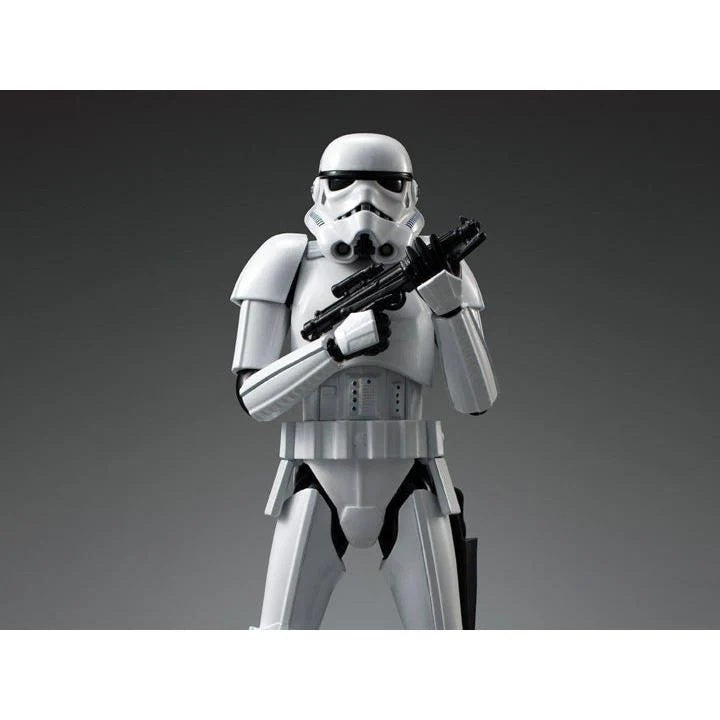 A white Stormtrooper action figure holding a black blaster, photographed against a dark gray gradient studio background.
