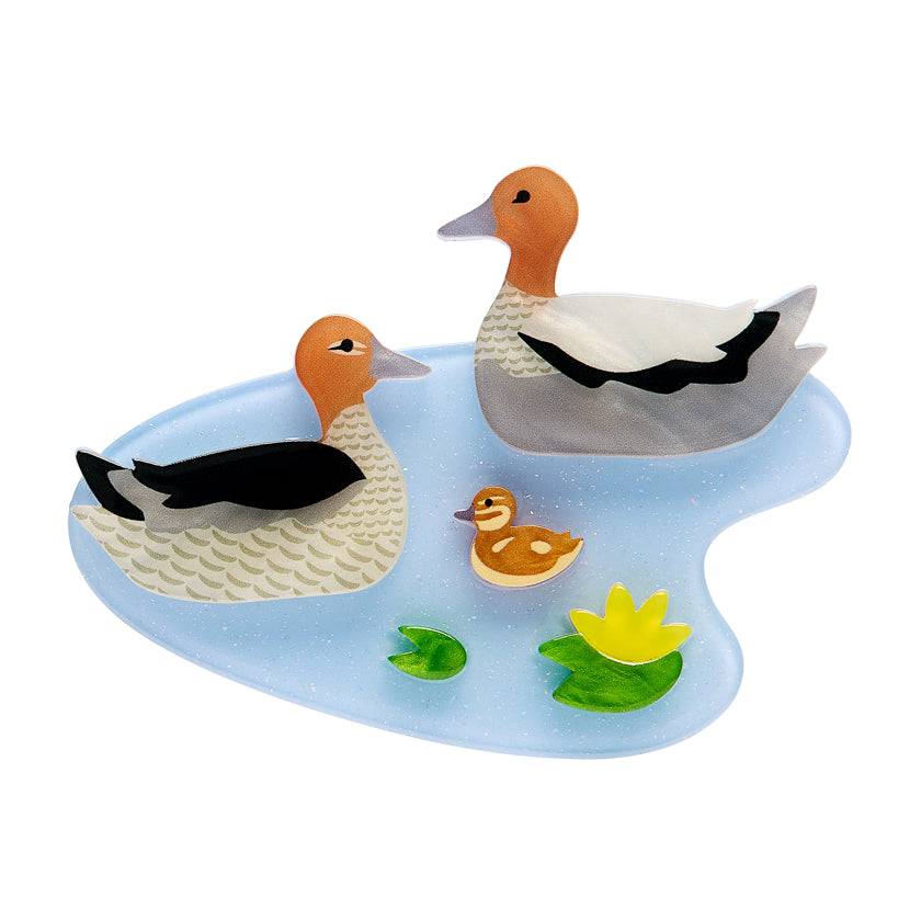 Erstwilder Brooch Featuring  a duck  family figures on a blue pond with lily flower & pads on a white background