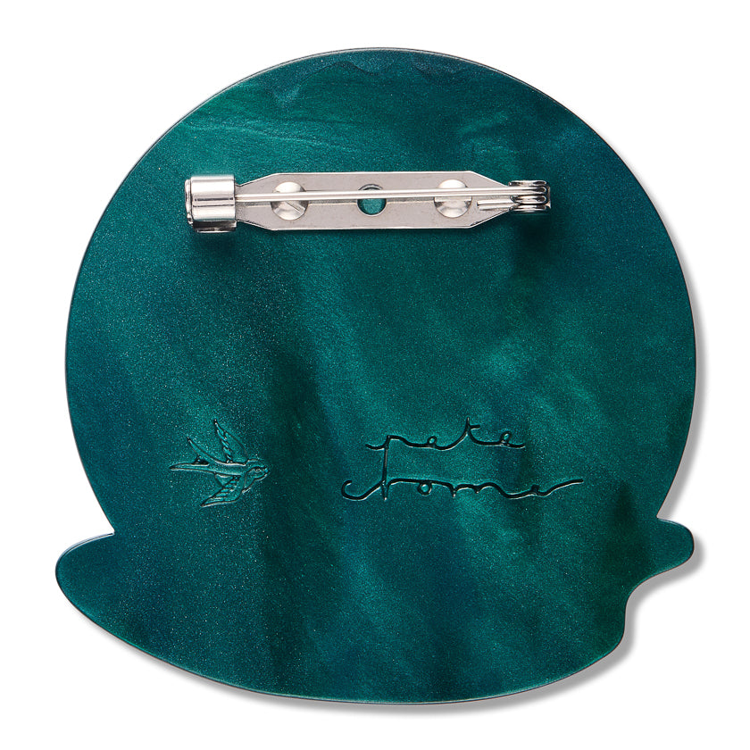 cack of Beauty sleep brooch Teal circular object with a metal clip on a white background