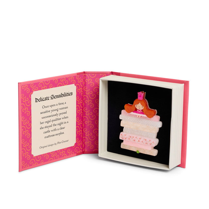 Book with a small illustration of a red-haired character on top of a stack of mattresses, surrounded by decorative text and patterns.