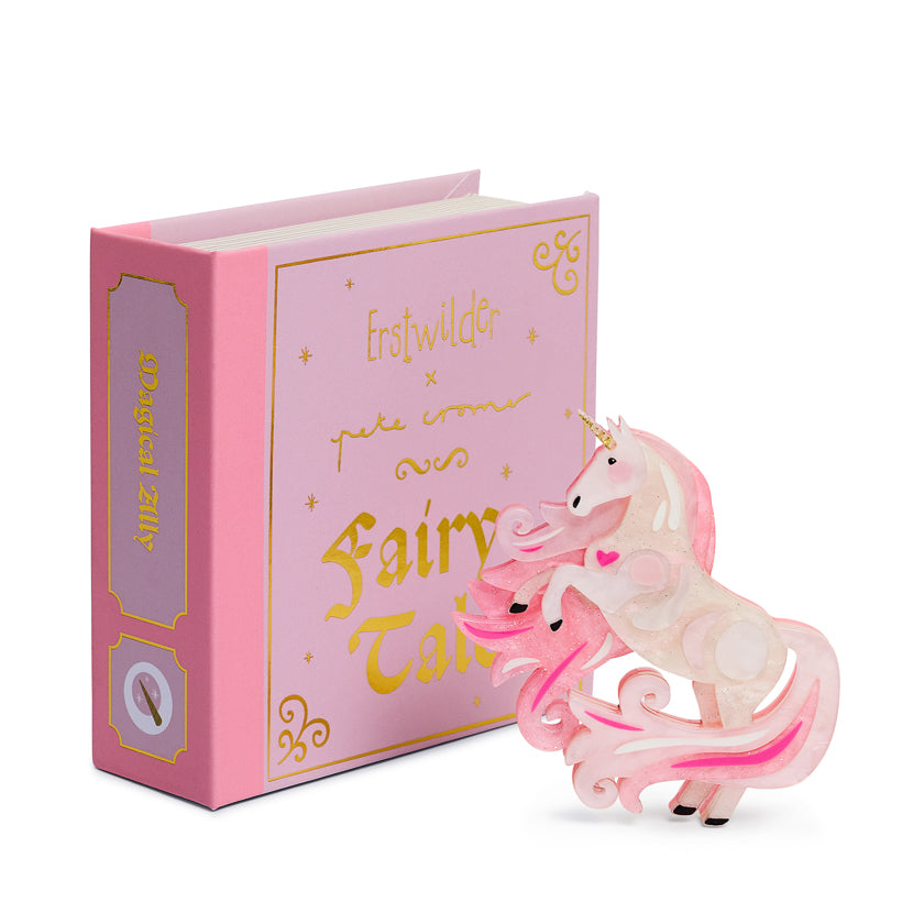 Pink unicorn figurine with a fairy on top of a pink book titled 'Fairy Tale'.