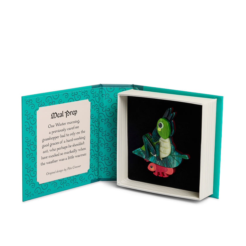 Open book with a small illustration of a green grasshopper sitting on a leaf carried by an ant on a black background, accompanied by a book shaped box  with text on it 
