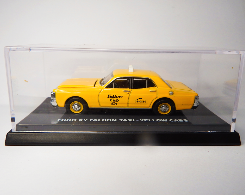 Model of a yellow taxi in a clear display case on a white background