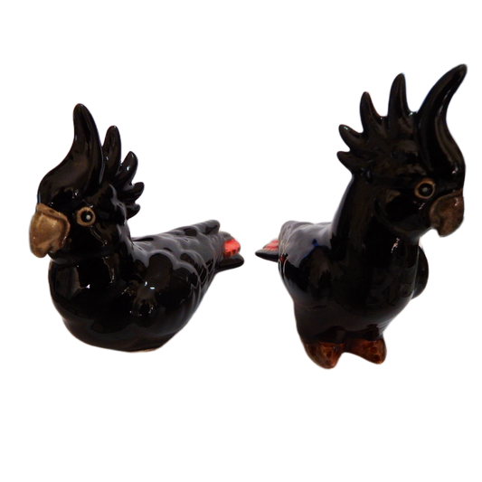 Two black red tail ceramic cockatoo figurines on a white background