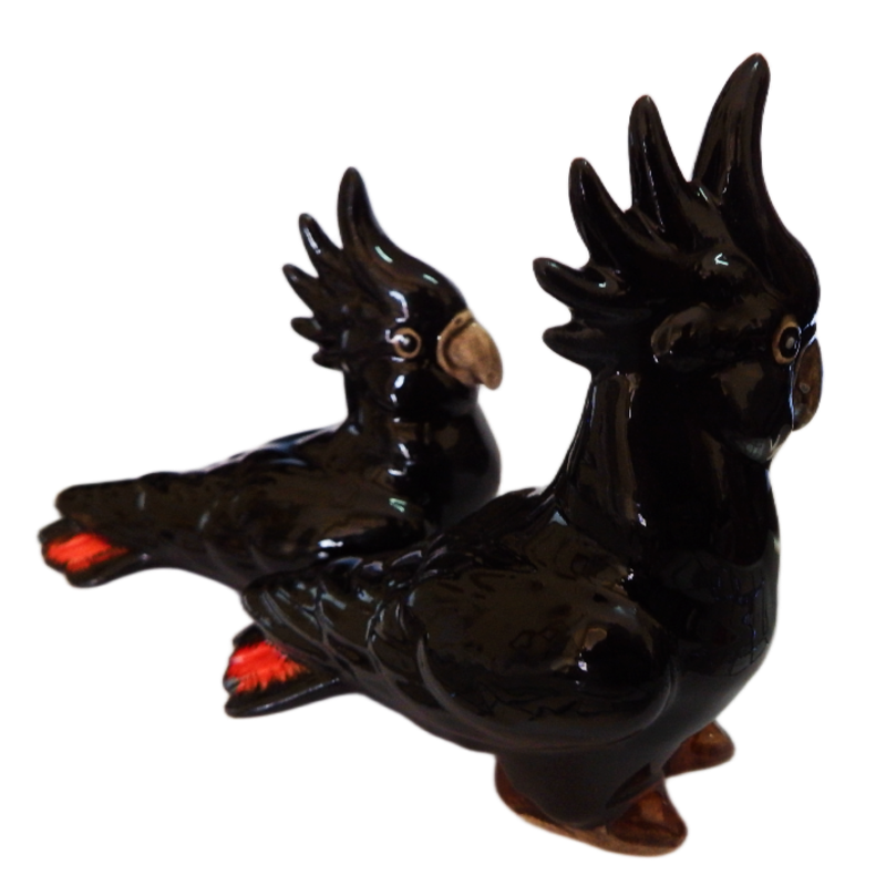 Two red tailed black ceramic cockatoo figurines on a white background