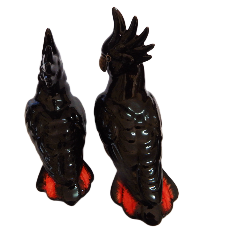 Two black cockatoo figurines with red accents on their tails a white background