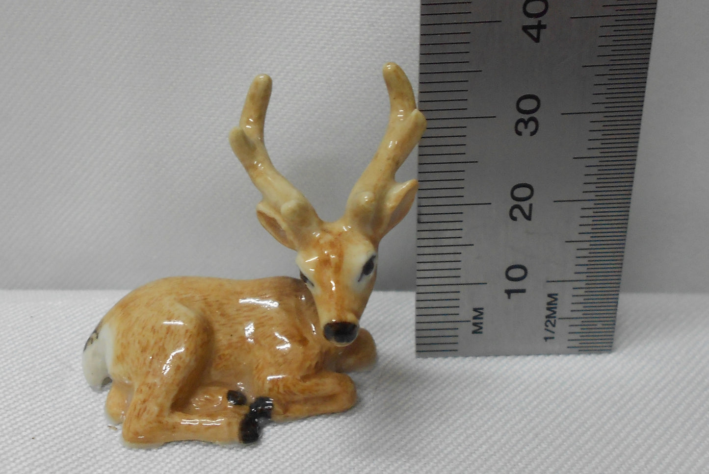 Small deer figurine next to a ruler on a white background