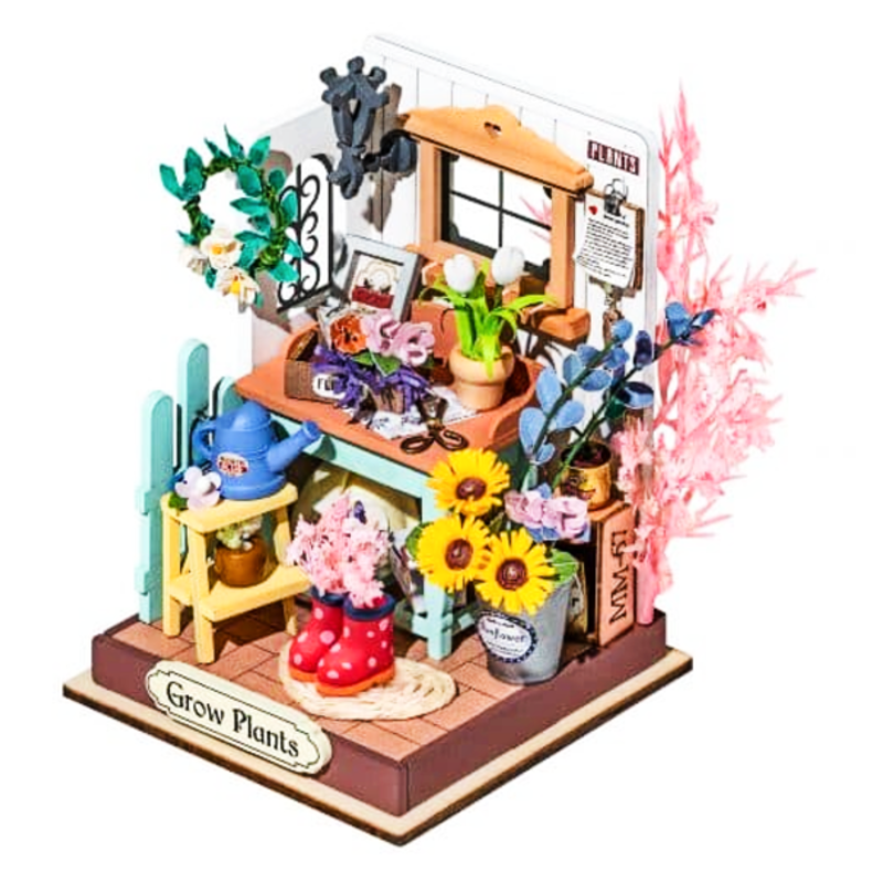 Miniature garden scene with plants, boots, and a watering can on a white background