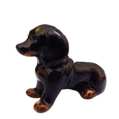 A glossy ceramic dachshund figurine in black with tan accents, shown against a plain white background.