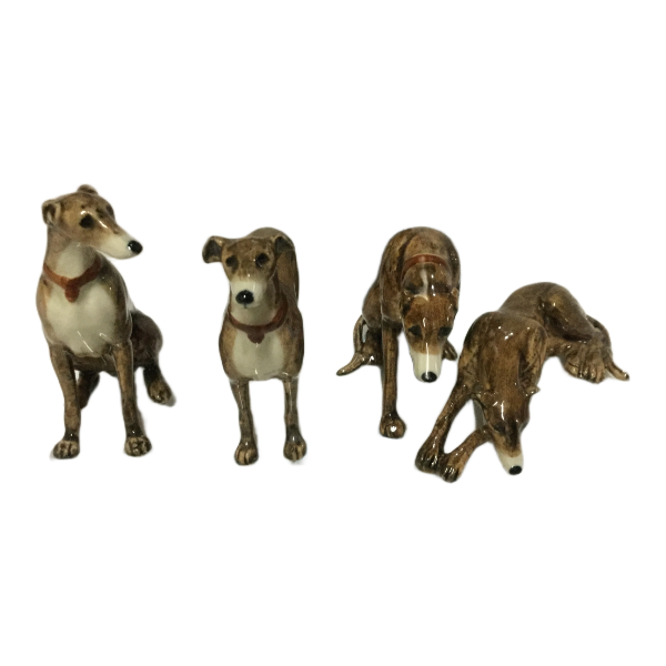 Four ceramic greyhound dog figurines in various poses, featuring brown and white glazes with reddish-brown collars, displayed against a plain white background.
