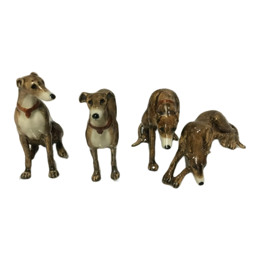 Four ceramic greyhound dog figurines in various poses, featuring brown and white glazes with reddish-brown collars, displayed against a plain white background.
