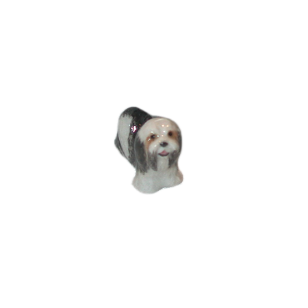 A small ceramic figurine of a long-haired dog, a maltese, with white, black, and tan fur, isolated on a white background.