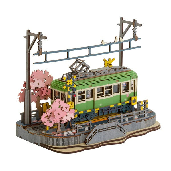 Model of a green train with cherry blossom trees and a station platform on a white background