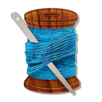 needle with blue thread  on a wooden reel a white background